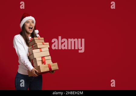 Holiday Offer. Excited Young Lady Wearing Santa Hat Holding Stack Of Gifts Stock Photo