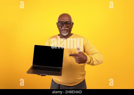 Happy senior black man pointing at laptop computer with black blank screen, showing copy space for your mockup Stock Photo