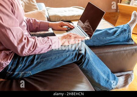 Side view of crop anonymous businessman sitting on sofa and typing on laptop while working at home Stock Photo