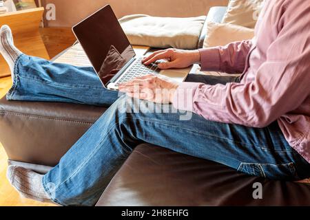 Side view of crop anonymous businessman sitting on sofa and typing on laptop while working at home Stock Photo