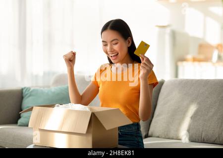 Delivery service and online payment concpet. Overjoyed asian lady opening box, making YES gesture, holding credit card Stock Photo