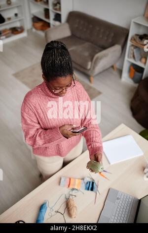 High angle portrait of young African-American woman taking photo of knitting wool and hobby supplies, copy space Stock Photo