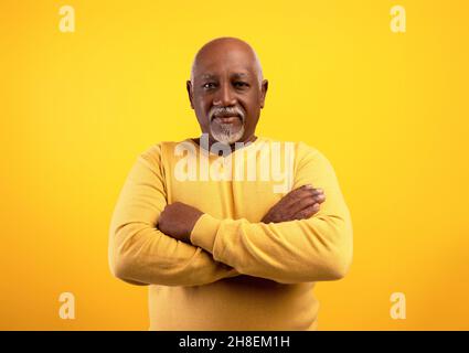 Portrait of positive senior African American man posing with crossed arms on orange studio background Stock Photo