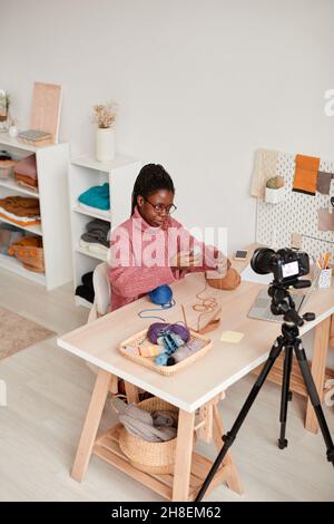 High angle portrait of young African-American woman knitting at home and recording video or livestream, copy space Stock Photo