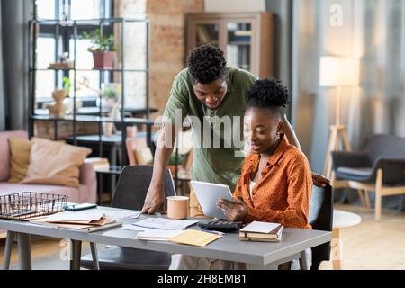 Smiling young African American couple using tablet app while planning family budget in living room Stock Photo