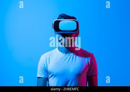 Bearded man using VR headset helmet to interacts with metaverse using swipe and stretching gestures. Watching virtual reality 3d video. Man in VR Stock Photo