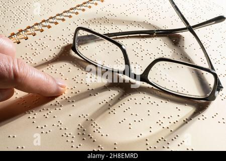 a pair of eyeglasses on a page written in Braille, the embossed tactile reading system for the blind Stock Photo