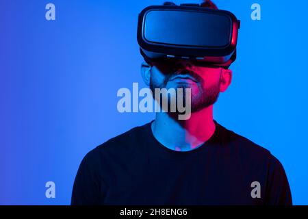 Bearded man using VR headset helmet to interacts with metaverse using swipe and stretching gestures. Watching virtual reality 3d video. Man in VR Stock Photo