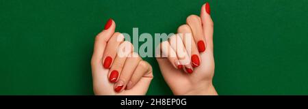Womans hands with trendy christmas red manicure on green background Stock Photo