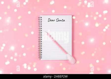 Letter to Dear Santa. Pink pen decorated with feather and Notepad isolated on pink background with golden tinsel. Holliday banner with copy space Stock Photo