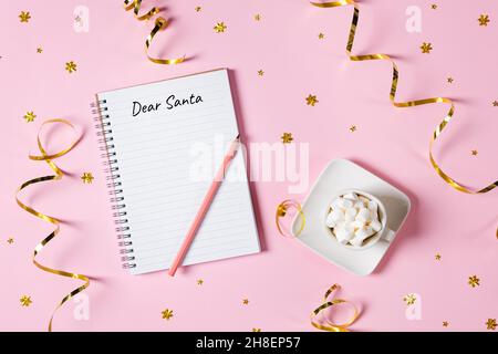 Letter to Dear Santa. Pink pen decorated with feather and Notepad isolated on pink background with cup of hot chocolate with marshmallows, a gift box Stock Photo