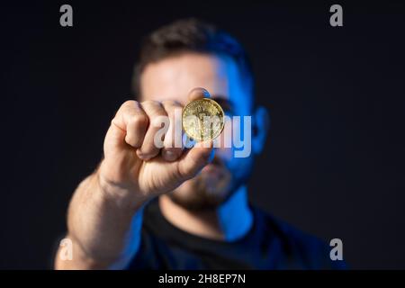 Mature bearded man wearing in black t-shirt holding gold bitcoin in hand and standing isolated on black background. Stock Photo