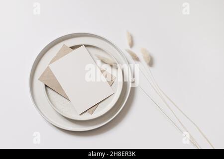 Modern autumn stationery still life. Blank greeting card mock up scene with Lagurus ovatus grass, craft envelope and ceramic plates isolated on white Stock Photo