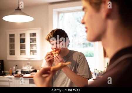 Teenage boys eating pizza in kitchen Stock Photo