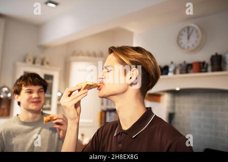 Hungry teenage boys eating pizza in kitchen Stock Photo
