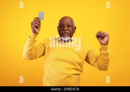 Elderly African American man showing credit card and making YES gesture on orange studio background Stock Photo