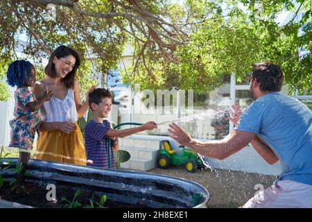 Happy family playing with hose in backyard Stock Photo