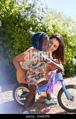 Mother helping cute toddler daughter ride bike Stock Photo