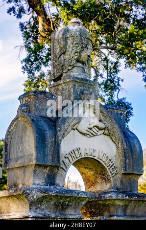 An ornate headstone features common funerary art symbols including clasped hands and a draped urn at Magnolia Cemetery in Mobile, Alabama. Stock Photo