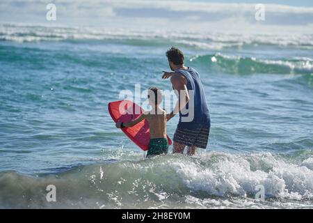 Father and son with body board watching ocean waves Stock Photo