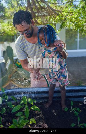 Father and toddler daughter watering plants in garden Stock Photo