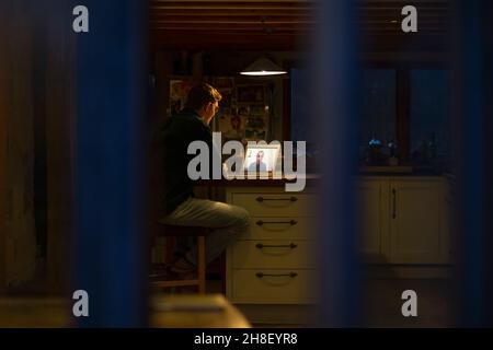 Man working late video conferencing at laptop in dark kitchen Stock Photo