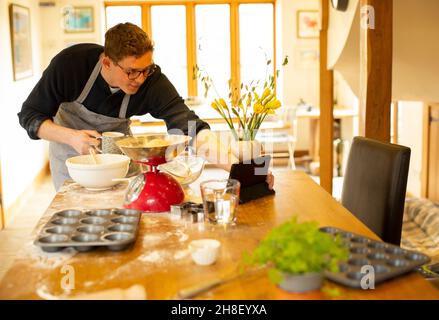 Man video chatting and baking in messy kitchen Stock Photo