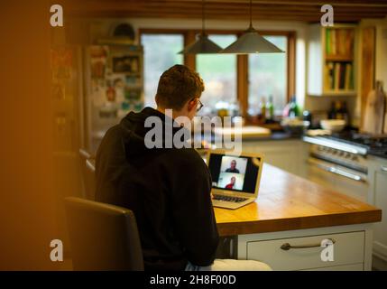 Man working at home video chatting with coworkers at laptop in kitchen Stock Photo