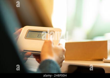 Woman adjusting thermostat at home Stock Photo