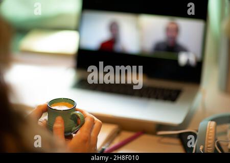 Woman with espresso video chatting with colleagues at laptop Stock Photo