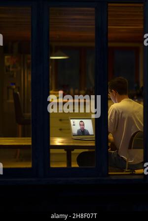 Man working late video conferencing with colleagues in dark kitchen Stock Photo