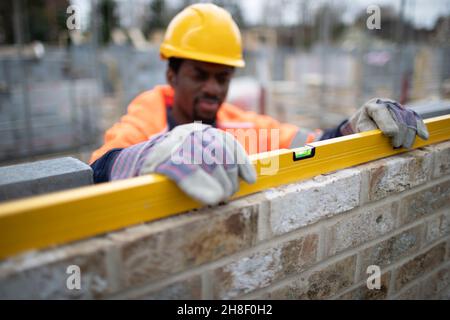 Male construction worker using level tool on brick wall Stock Photo