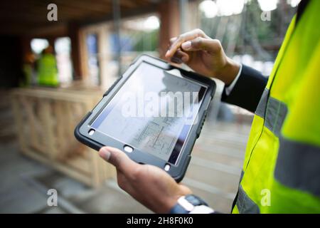 Male architect looking at blueprints on digital tablet Stock Photo