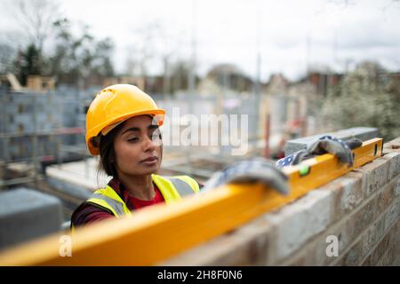 Female construction worker using level tool on brick wall Stock Photo
