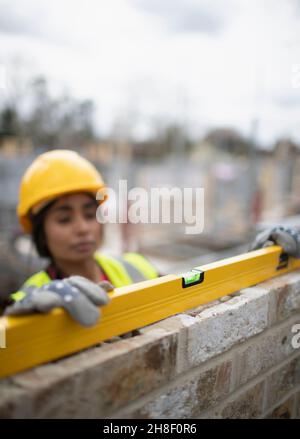 Female construction worker using level tool on brick wall Stock Photo