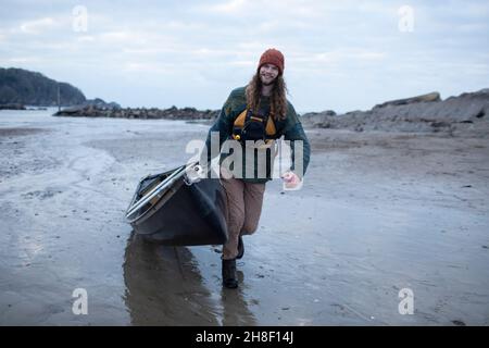 Portrait young man pulling canoe on wet sand beach Stock Photo