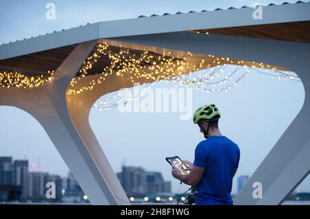 Man in helmet using digital tablet below illuminated bridge, London Stock Photo