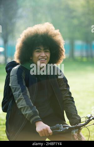Portrait happy young man with afro on bicycle in park Stock Photo