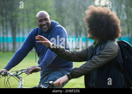 Happy father and teen son riding bikes in park Stock Photo