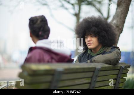 Young man with afro talking to sister on park bench Stock Photo