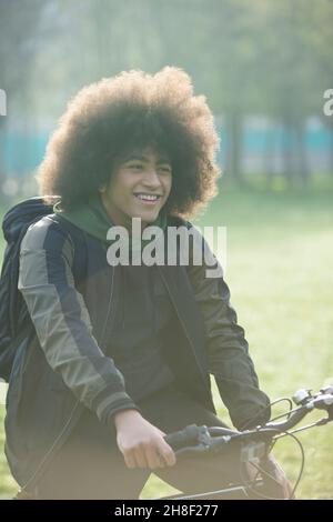 Happy young man with afro on bicycle in park Stock Photo
