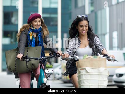 Happy young women friends riding bicycles in city Stock Photo