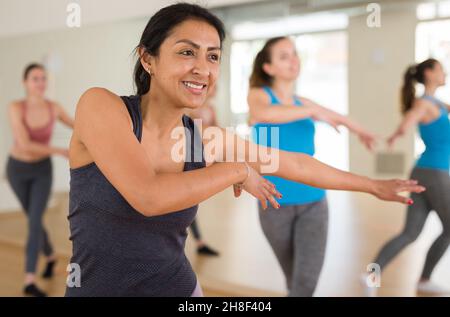 Cheerful hispanic woman practicing vigorous dance in group class Stock Photo