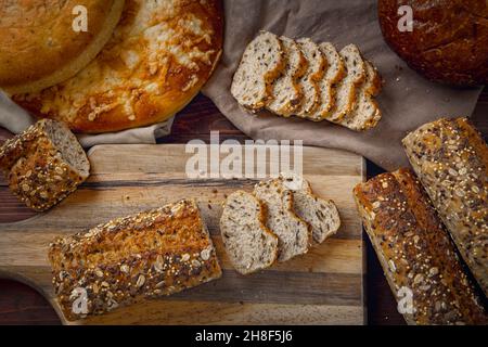 An overview of a baguette on a cutting board surrounded by various types of breads. Stock Photo