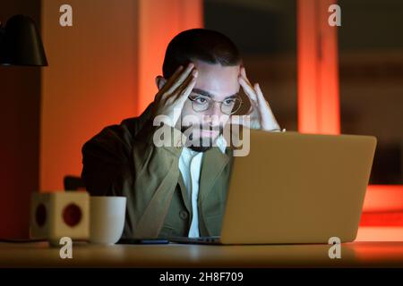 Stressed tired businessman work late at night in office try to find solution to project problem Stock Photo