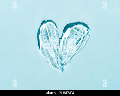 Liquid gel cosmetic smudge texture in heart shape on blue background. Aesthetic beautiful textured smear transparent skin gel or face mask like heart. Top view or flat lay Stock Photo