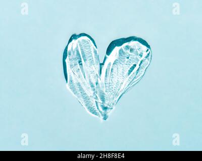 Liquid gel cosmetic smudge texture in heart shape on blue background. Aesthetic beautiful textured smear transparent skin gel or face mask like heart. Top view or flat lay Stock Photo