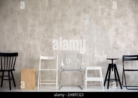 Wooden plastic and metal chairs placed in row near cement wall in studio Stock Photo