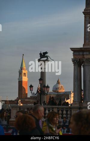 a view of the bronze statue in san marco square of the winged lion over a column with the bell tower of Saint Georges Church in the background Stock Photo