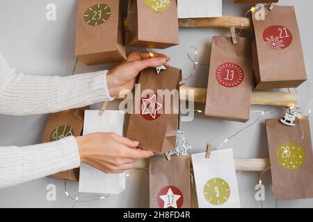 Hanging DIY handmade craft Christmas advent calendar with gifts. Mother preparing festive decor and tradition for kids. Bags with dates on eco tree Stock Photo